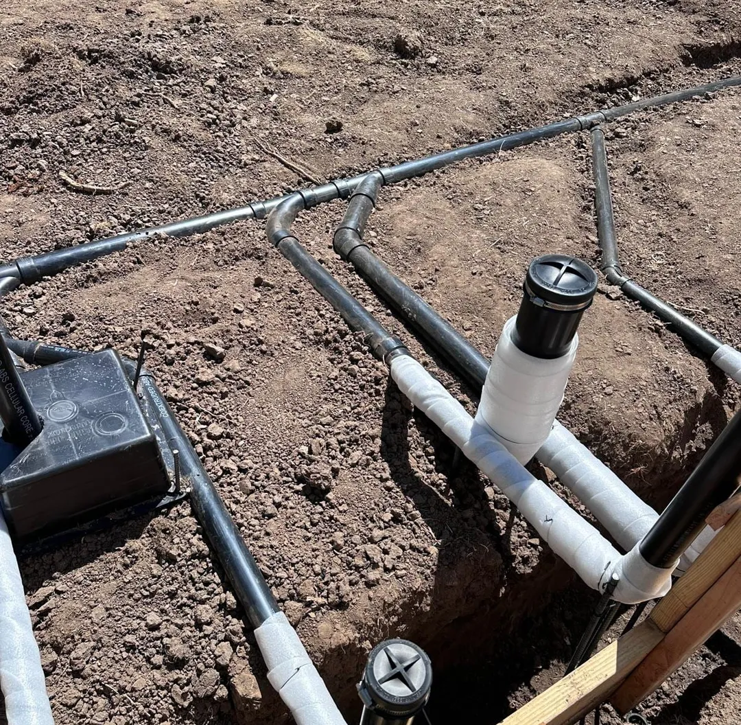 Underground drain lines with white cleanout risers and a valve box in an open trench