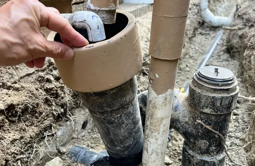 Cast-iron sewer cleanout opened at the side of a house, tree roots in the trench around it