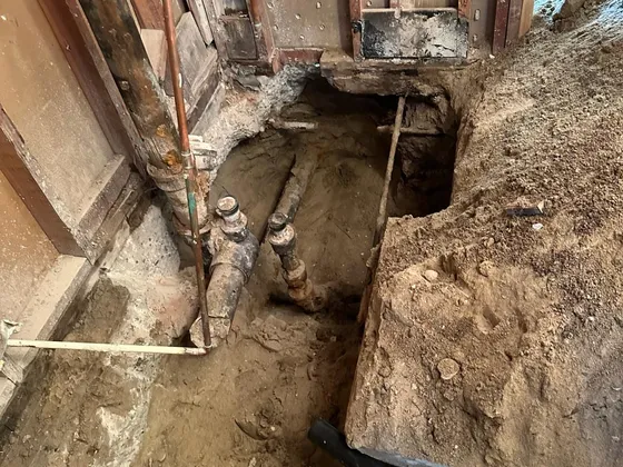 An opened section under a house floor exposing an old drain line next to new black pipe