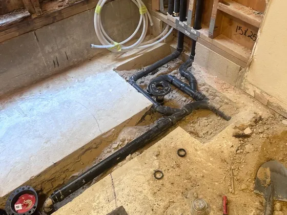 New black drain lines laid in a trench cut through a bathroom slab, with a capped toilet flange