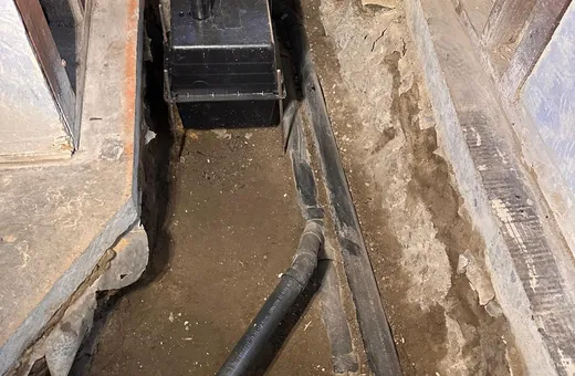 Open trench under a house slab with new drain pipe run and a work light in the background