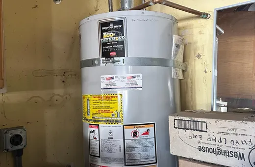 Gas water heater in a garage with earthquake straps, code labels and the install date written on the tank